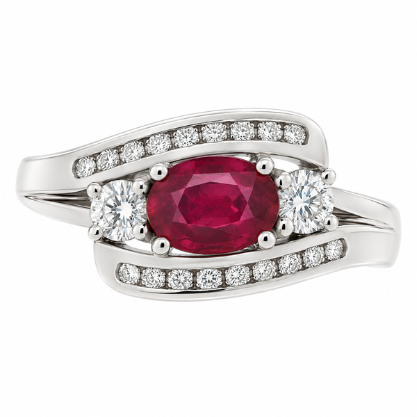 Designer style trilogy dress ring with oval ruby, two accent round brilliant cut diamonds and channel set round diamonds in the crossover shoulders platinum gold